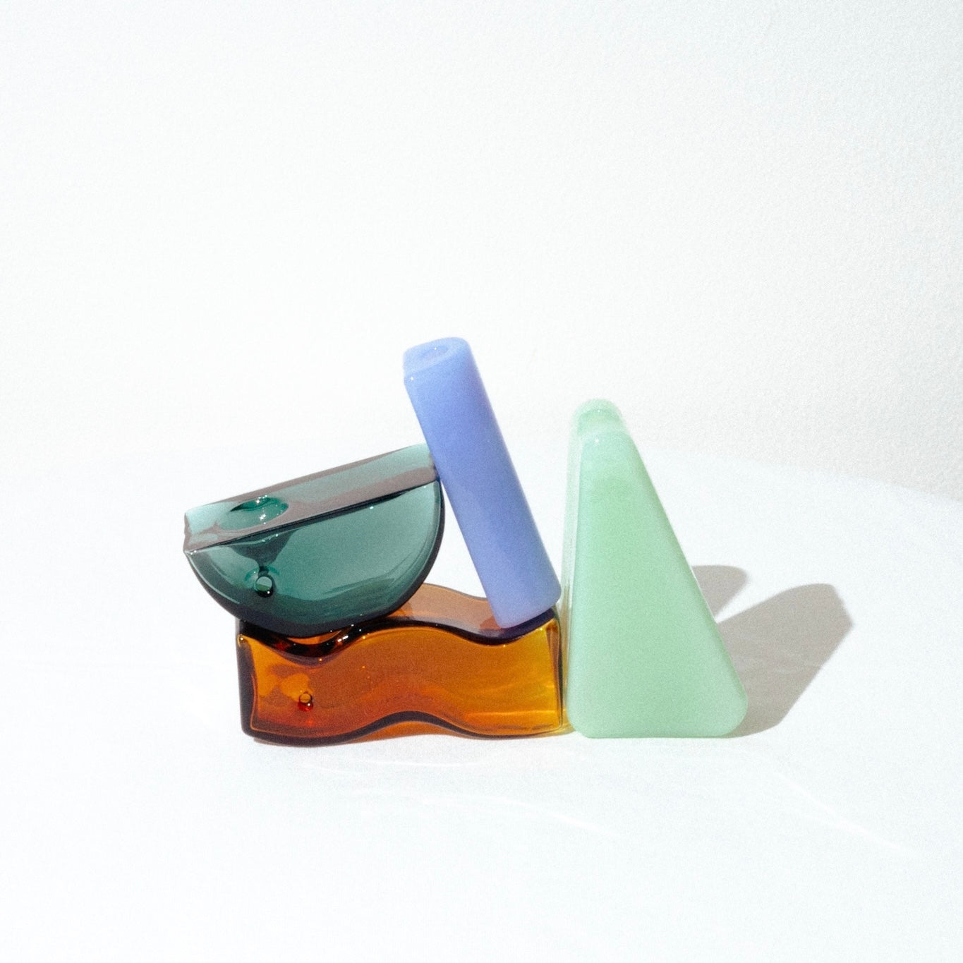 image of 4 yew yew glass pipes. a tubular solo pipe on the left in a milky blue, the amber wavy pipe, the green triangle pipe and then the teal half circle pipe. they are all either upright or on their side, in a formation