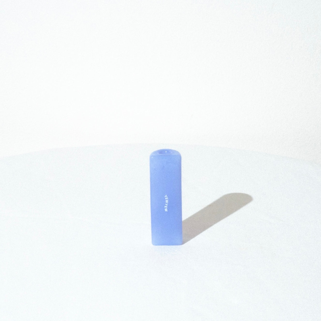 the yew yew solo pipe in milky blue on a white table, and a white background. we can see the flat side of the pipe with the logo on it. 