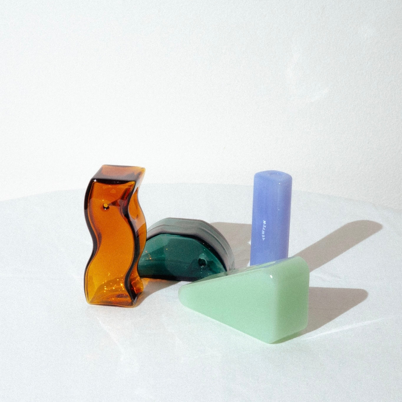 image of 4 yew yew glass pipes. a tubular solo pipe on the left in a milky blue, the amber wavy pipe, the green triangle pipe and then the teal half circle pipe. they are all in different positions against a white background.
